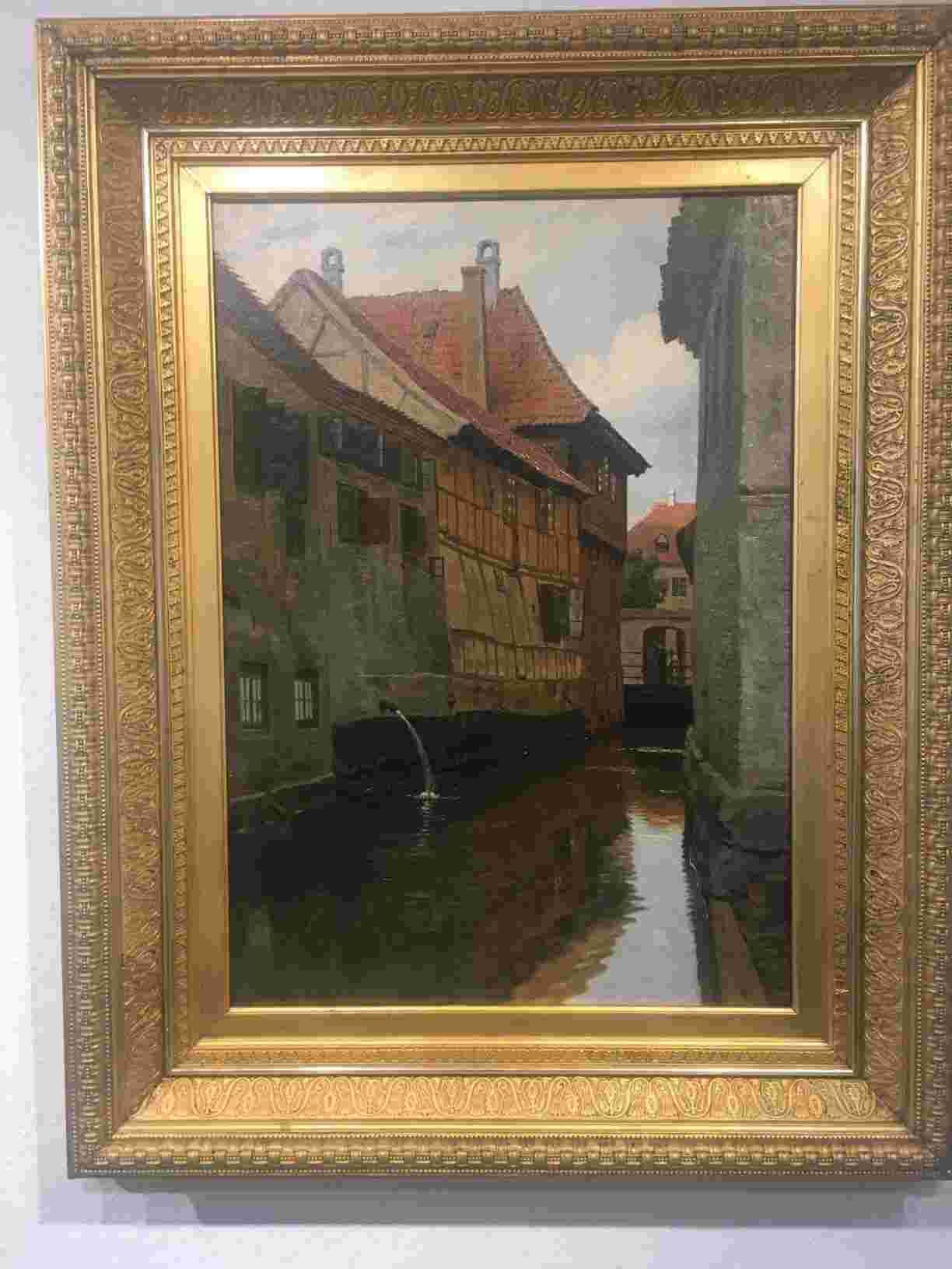 Johannes August Fischer (1854-1921) kendes især som arkitekturmaler. Motiverne er gamle, maleriske huse og by partier, ofte fra udlandet, f.eks. Nürnberg, Rothenburg, Hamborg, Lübeck, Venedig og Firenze. De danske motiver fandt han hovedsageligt i Ribe, bl.a. i perioden 1918 -1919 - men også motiver fra Ebeltoft og København er blandt hans motivverden.  Den yngre bror Paul Fischers, med de velkendte Københavnermotiver, syntes på de udenlandske kunstauktioner i 1980erne at have smittet af på den ellers generelt lidt oversete, men meget dygtige maler. August Fischer, Parti fra Ribe med huse og stille vand. Monteret i kraftig guldramme. Meget flot stand. 60 x 75 cm. Pris: Kontakt