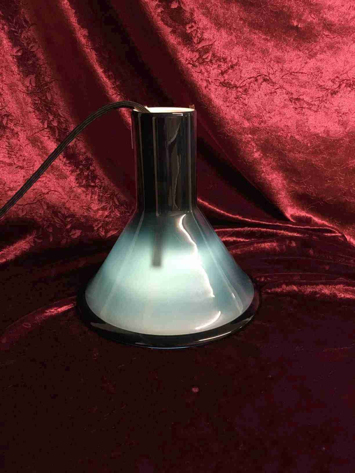 Holmegaard P&T pendel i mundblæst glas, designet af Michael Bang i 1972, skærm af petroliumsblå overfangs glas, som virker sort når lyset ikke er tændt, indvendig hvidt opalglas, med originalt ledningsophæng og fatning. Perfekt stand. Pris: 1.200, - Kr.