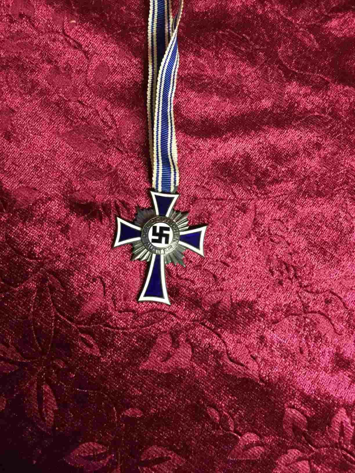 Military - 24-1071-380-B - Den 16. december 1938 indførte Adolf Hitler prisen Mother's Cross, den tyske moders æreskors. Fortjenstmedaljen blev uddelt årligt den anden søndag i maj (mors dag) og den 12. august på Klara Hitlers (Hitlers mor) fødselsdag. Oprindeligt var det kun mødre over 60, der kunne indstilles, men efter 1940 blev det besluttet at ændre dette, så også yngre mødre med mange børn kunne modtage fortjenstmedaljen. Prisen bar påskriften "Den tyske moder" og oprindeligt også "Barnet forædler mor". Medaljerne blev kun uddelt til genetisk sunde og sunde etnisk tyske mødre mellem årene 1939-1945, og var i bronze-, sølv- og guldklasserne. Et bronzekors blev givet til mødre med fire eller fem børn, sølv til mødre med seks eller syv børn og guld til mødre med otte eller flere børn. Anbefalinger til moderkorset ankom på en fast dag i begyndelsen af hver måned til kancelliet i Berlin, som stod for fortjenstmedaljen. Derfra kunne sagen tages op af den lokale borgmester eller efter anmodning fra NSDAP's lokale ledere eller det svenske børnefamilieforbund. Tyske familier blev opfordret til at få mange børn, og staten traf flere foranstaltninger for at støtte dette. De indførte blandt andet hvilehjem, hvor tyske mødre kunne aflaste sig og hvile, mens familierne fik tildelt en barnepige. Allerede efter magtovertagelsen i 1933 indførte regeringen loven om tilskyndelse til ægteskab. Det betød, at nygifte unge par fik et lån på 1.000 mark, hvilket dengang svarede til cirka ni måneders løn. Hvis parret fik et barn, blev gælden nedsat med 25 %, med to børn 50 % og med fire børn 100 %. Det var ikke kun gifte mødre, der blev tildelt Moderkorset. Selv enlige mødre kunne få det, hvilket dengang var et radikalt syn på kvinder med børn. Hitler var meget omhyggelig med at understrege vigtigheden af ikke at udstøde disse kvinder fra samfundet eller skamme dem. Det tyske velgørenhedsprogram ”Lebensborn”, som blev skabt på initiativ af SS, er yderligere et bevis på den radikale nationalsocialistiske kvindepolitik. Der kunne især enlige mødre og sårbare gravide få hjælp. Moderkorset var en del af denne meget succesrige socialpolitik, hvis formål var at fremme det voksende tyske folk. I den nationalsocialistiske ideologi anses moderen og den blomstrende familie som en væsentlig del af racens fundament. Tysk moderkors i sølv (6 eller syv børn) i super flot stand. Pris: 400,- Kr.