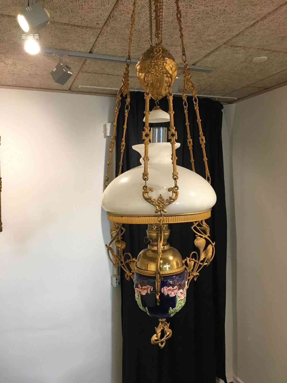 Olielampe Majolika hængelampe ca. 1880, ophæng af guldbronceret metal. Blå bund bemalet med blomster, skærm af hvid opalglas, med rør og røgfanger. Flot stand. Pris: 2.500,- Kr.